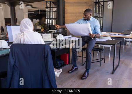 Diverse architects working on blueprint at open-plan office desk with laptop, copy space Stock Photo