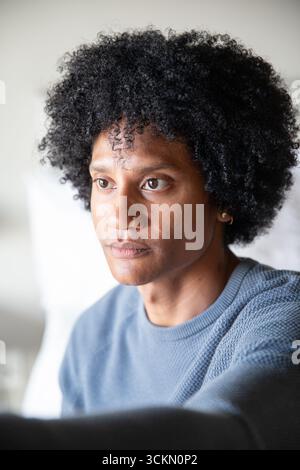 African american man sitting on sofa in living room in light blue sweater by white cushion Stock Photo