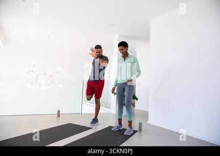Diverse workout partners balancing on yoga mats in living room with chandelier and potted plant Stock Photo