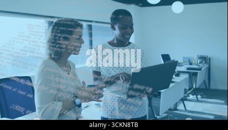 Reviewing code two mid adult women standing in open plan office, with laptop computer Stock Photo