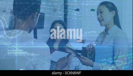 Gesturing Korean businesswoman holding laptop folder at desk, monitors, floating charts, copy space Stock Photo