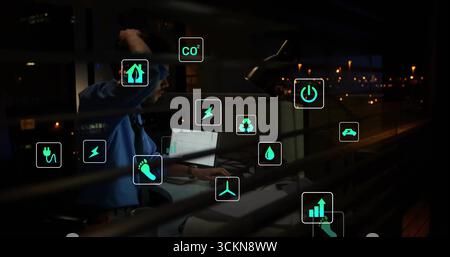 Reviewing engineer in tie monitoring laptop with eco icons at night office view, copy space Stock Photo