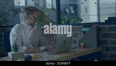 Man wearing white shirt reviewing documents on laptop at office desk, with succulent, copy space Stock Photo