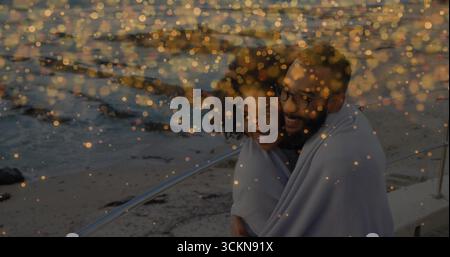 Leaning against metal railing at seaside promenade, woman and man wrapping in light-colored blanket Stock Photo