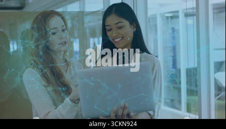 Collaborating two tech professionals wearing blazer examining laptop in office with network overlay Stock Photo