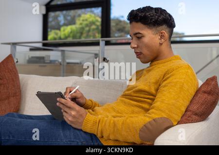 Man in twenties sitting on sofa using stylus on tablet, copy space Stock Photo