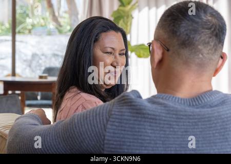 Senior asian father and daughter sitting on sofa in living room among throw pillows Stock Photo