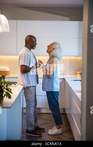 Diverse couple standing holding hands and gazing at each other in kitchen with countertop island Stock Photo