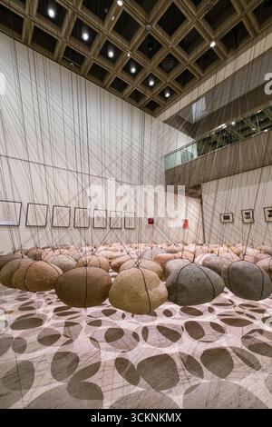 Dynamic art installation featuring suspended stones connected by strings creating intricate patterns, displayed in a modern art gallery setting with g Stock Photo