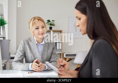 Two successful businesswomen sitting together in office, looking through paper documents Stock Photo