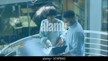 Standing colleagues analyzing laptop next to papers on interior balcony railing, with data overlay Stock Photo