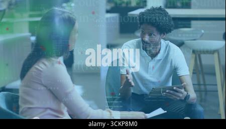 Discussing mid-adult professionals holding tablet and document in break area with code overlay Stock Photo