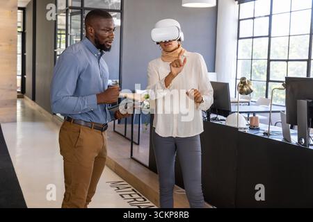 Diverse coworkers wearing vr headset, holding tablet interacting with interface at modern office Stock Photo