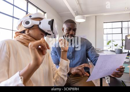 Diverse colleagues collaborating on design review in bright office with vr headset, blueprints Stock Photo