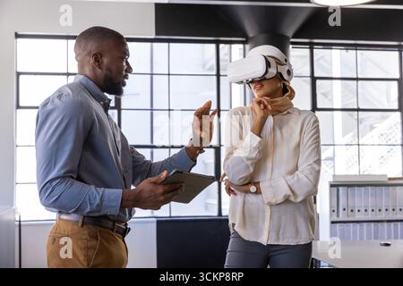 Diverse coworkers presenting virtual reality with vr headset, tablet at desks in office Stock Photo