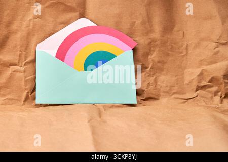 Green envelope with a rainbow-shaped card on a cardboard textured background. Stock Photo