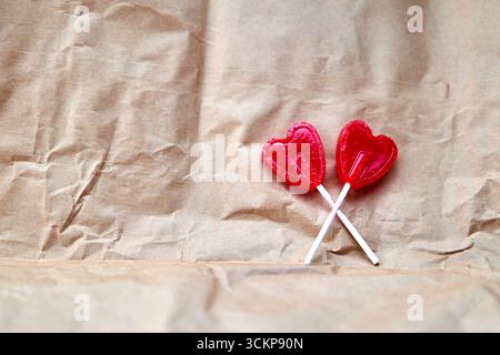 Two red heart-shaped lollipops together on a cardboard background. Stock Photo