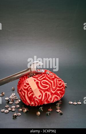 Wrench on top of a red human brain with a dark background, concept of breaking mental barriers Stock Photo