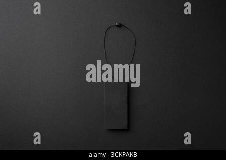 Minimalist black cardboard clothing tag with string on dark background Stock Photo