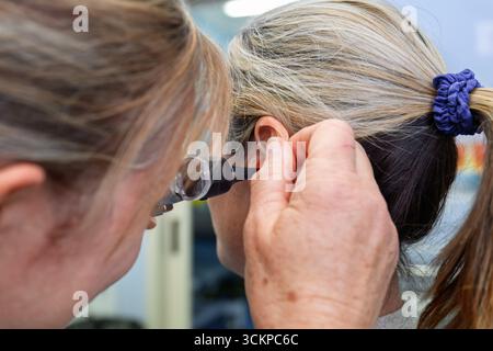 female doctor nurse using otoscope to examine patient ear, general practice, medical clinic, hospital health setting Stock Photo