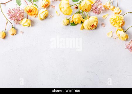 Yellow roses and pink hydrangea flowers on light stone background, flat lay floral frame with copy space, pastel tones for wedding invitation Stock Photo