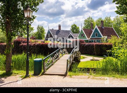 A wooden footbridge leads to the Overtuin garden lined with historic wooden houses in the Zaanse Schans quarter on a sunny spring day. Stock Photo
