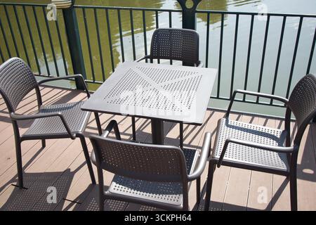 A wooden deck with a table and chairs. The table is square and has a metal top. There are five chairs around the table. The chairs are all black and h Stock Photo