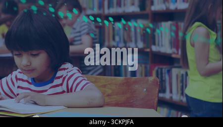 Girl in striped T-shirt reading open book at wooden table in library, with bookshelves, copy space Stock Photo