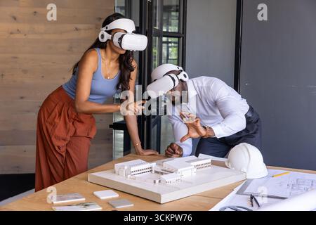 Diverse colleagues wearing vr headsets pointing at scale model blueprints in design studio Stock Photo