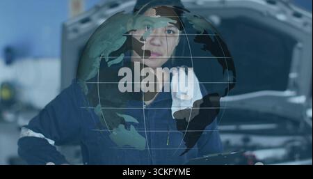 Mechanic scanning engine under hood in bay, wearing coveralls and holding tablet with globe overlay Stock Photo