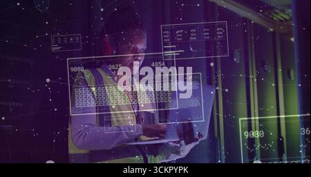 Standing technician wearing safety vest, earmuffs in rack aisle, using laptop showing data overlays Stock Photo