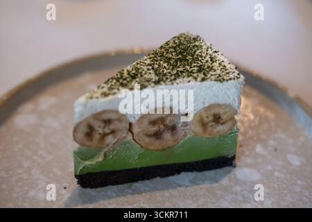 Matcha green tea banoffee pie, served on plate. It is a dessert made from banana, whipped cream, thick caramel sauce with crumbled base. Stock Photo