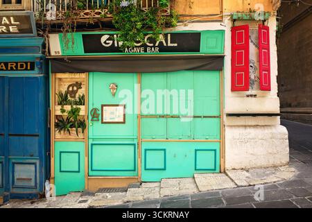 Valletta, Malta - 08.26.2025: Facade of a bar with a turquoise door and red shutters on the corner of an old house decorated with creative street art. Stock Photo