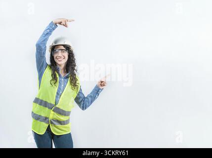 Smiling female builder pointing an advertisement isolated. Beautiful female engineer pointing to the side with both fingers isolated Stock Photo