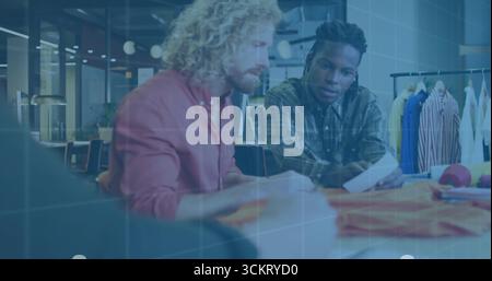 Two designers leaning over table selecting fabric swatches in design studio, with garment samples Stock Photo