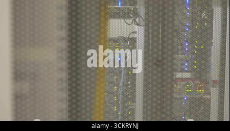 Showing rack behind perforated door in data center, featuring network switch modules blinking LEDs Stock Photo