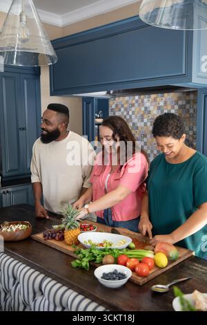 Diverse friends chopping pineapple and grapes on wooden cutting board at kitchen island at home Stock Photo