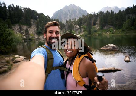 Happy couple hiking by a mountain lake, taking a selfie Stock Photo
