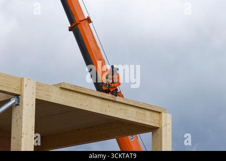 Glulam timber frame with workman on roof using cordless drill, mobile crane in background on Bury flexi hall construction site, greater manchester uk Stock Photo