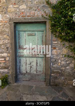 An old wooden heavy door with fading paintwork and peeling off, attached to an old water mill in Tuscany, Italy Stock Photo