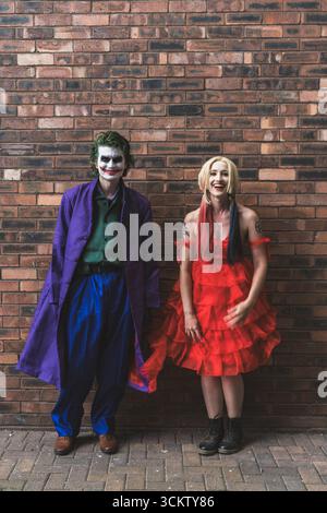 A pretty girl and handsome male cosplayer having fun and laughing whilst dressed as The Joker and Harley Quinn with copy space above Stock Photo