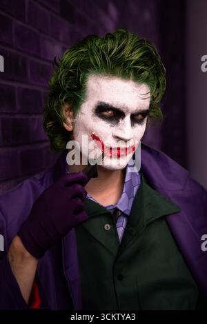 Close up portrait of a young male cosplayer dressed as The Joker with a knife and smile looking serious and directly at the camera with copy space Stock Photo