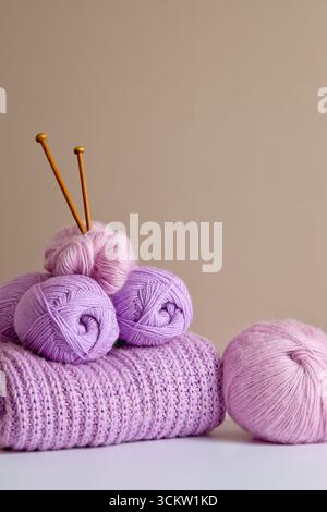 Purple and pink yarn balls with knitting needles and folded knitted sweater. Stock Photo