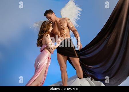 Two models in angelic costumes pose together against a blue backdrop Stock Photo