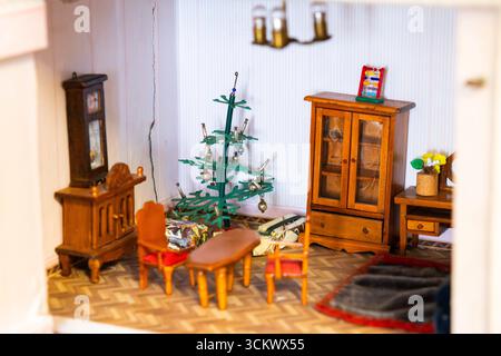 Miniature living room showcasing festive Christmas decorations, wooden furniture, and wrapped gifts under a charmingly decorated Christmas tree Stock Photo