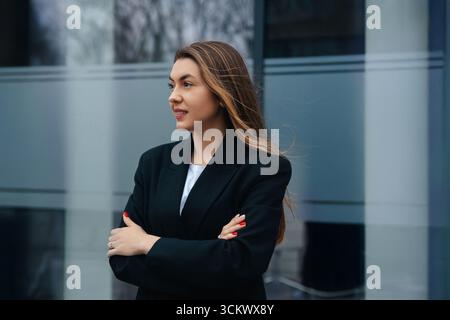 Young woman in a fashionable black blazer stands confidently with arms crossed, embodying modern style and professionalism, exuding empowerment Stock Photo