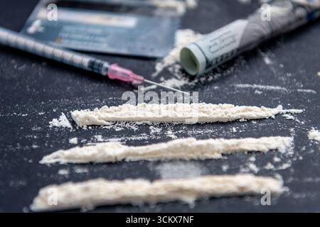 An illegal drug taking, addiction concept with white plain flour divided into three rows using a bank card, a medical syringe, and a rolled up 100 US Stock Photo