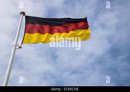 German national flag fluttering in the wind against a clear sky, black, red, and gold stripes symbolising Germany, unity, and national pride. Stock Photo