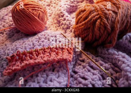 Red Ball Of Wool And Small Knitted Piece With Lace Pattern With Knitting Needles On Violet Knitted Scarf. Concept Handicraft, Hobby, Knitting Stock Photo
