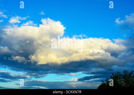 Large yellow cloud before storm against blue sky during evening light Stock Photo